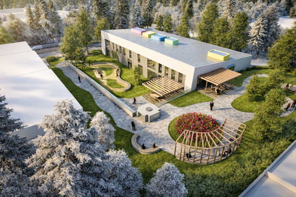 Modernes, rechteckiges Gebäude mit farbenfrohen Dachkonstruktionen, umgeben von üppigem Grün und schneebedeckten Bäumen. Menschen schlendern auf geschwungenen Wegen, Sitzgelegenheiten und Blumenbeete schaffen eine ruhige Atmosphäre.